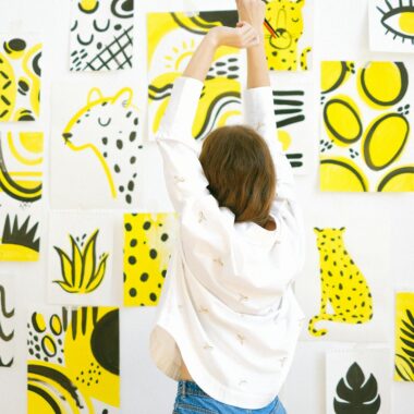 Creative woman paints abstract yellow art pieces on a white wall in a modern studio.